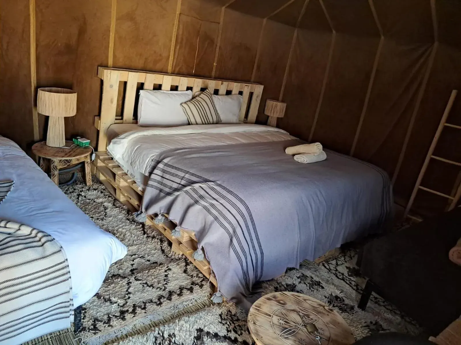 Double tent room at Hassan desert camp in Merzouga with a large bed, single bed, and rustic wooden headboard