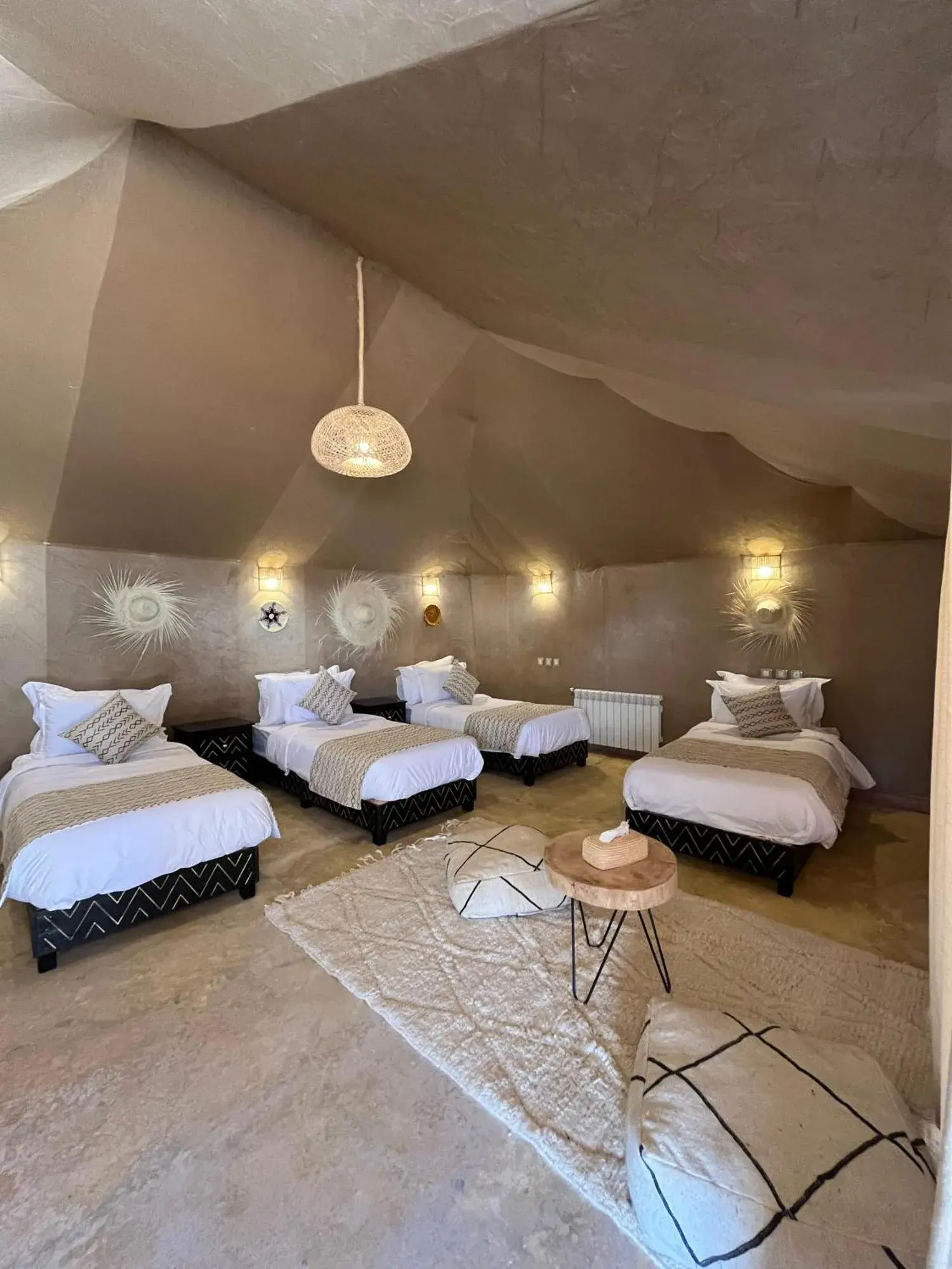 Shared tent room at Hassan desert camp in Merzouga with four single beds, woven decor, and warm ambient lighting