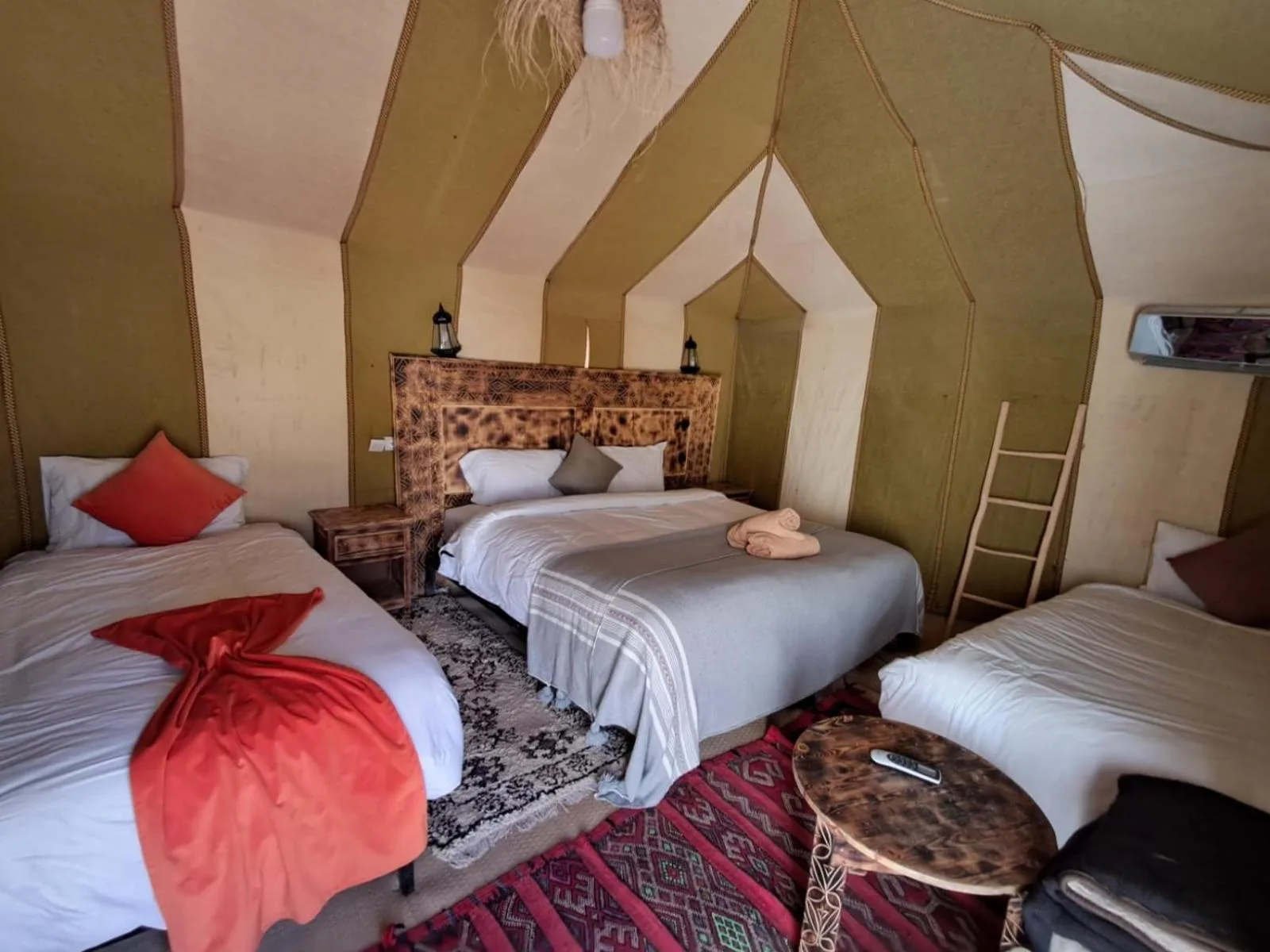 Tent bedroom at Hassan desert camp in Merzouga with a double bed, single bed, and warm ambient lighting
