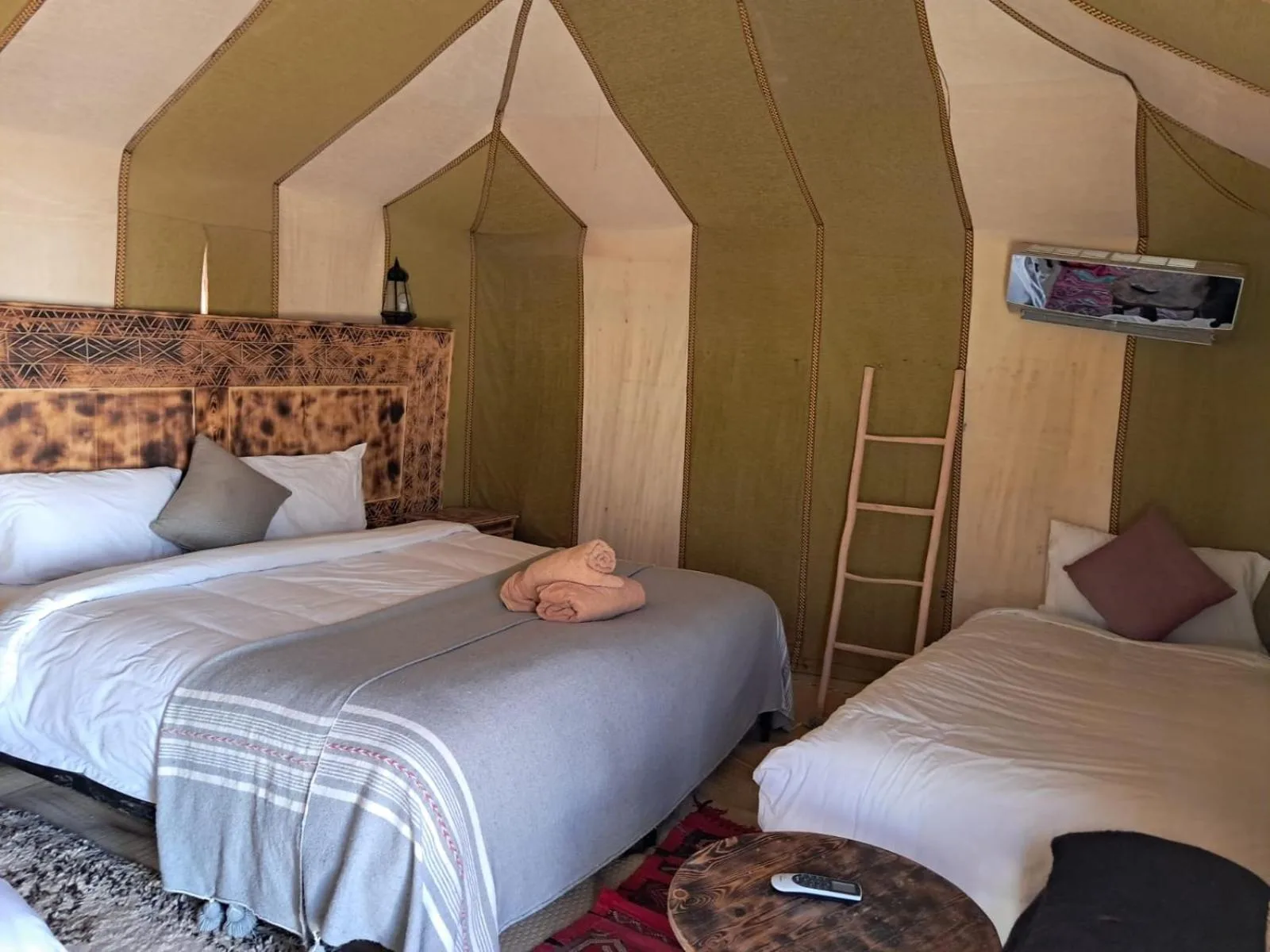 Triple tent room at Hassan desert camp in Merzouga with three beds, patterned rugs, and traditional tent walls