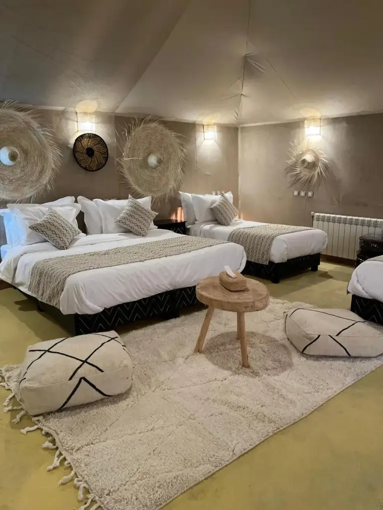 Twin tent room at Hassan desert camp in Merzouga with a large bed, single bed, textured rugs, and traditional wall decor