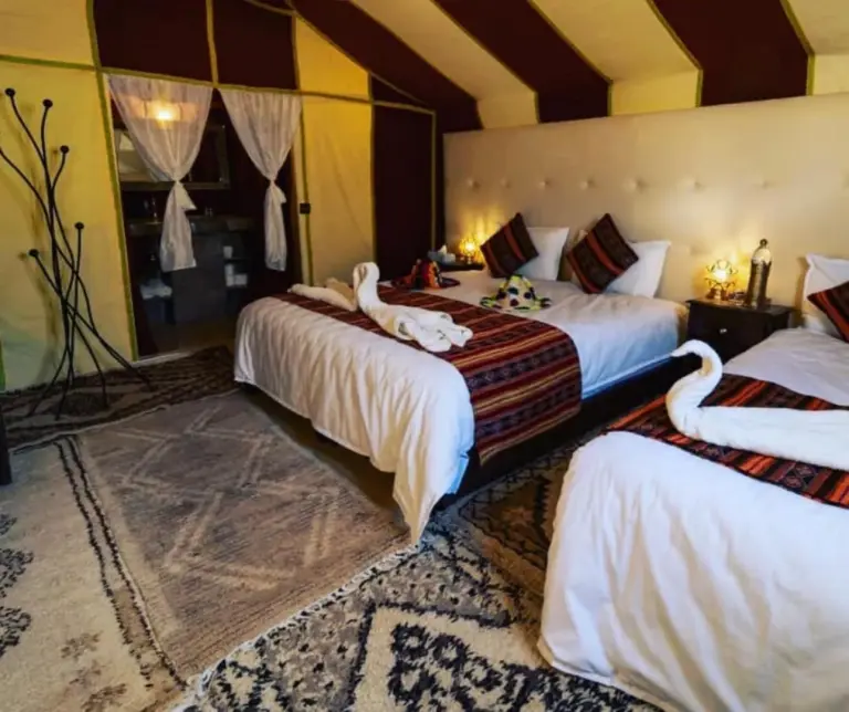 Elegant suite interior at Holiday Desert Camp in Merzouga with large bed, twin bed, lamps, and patterned rugs
