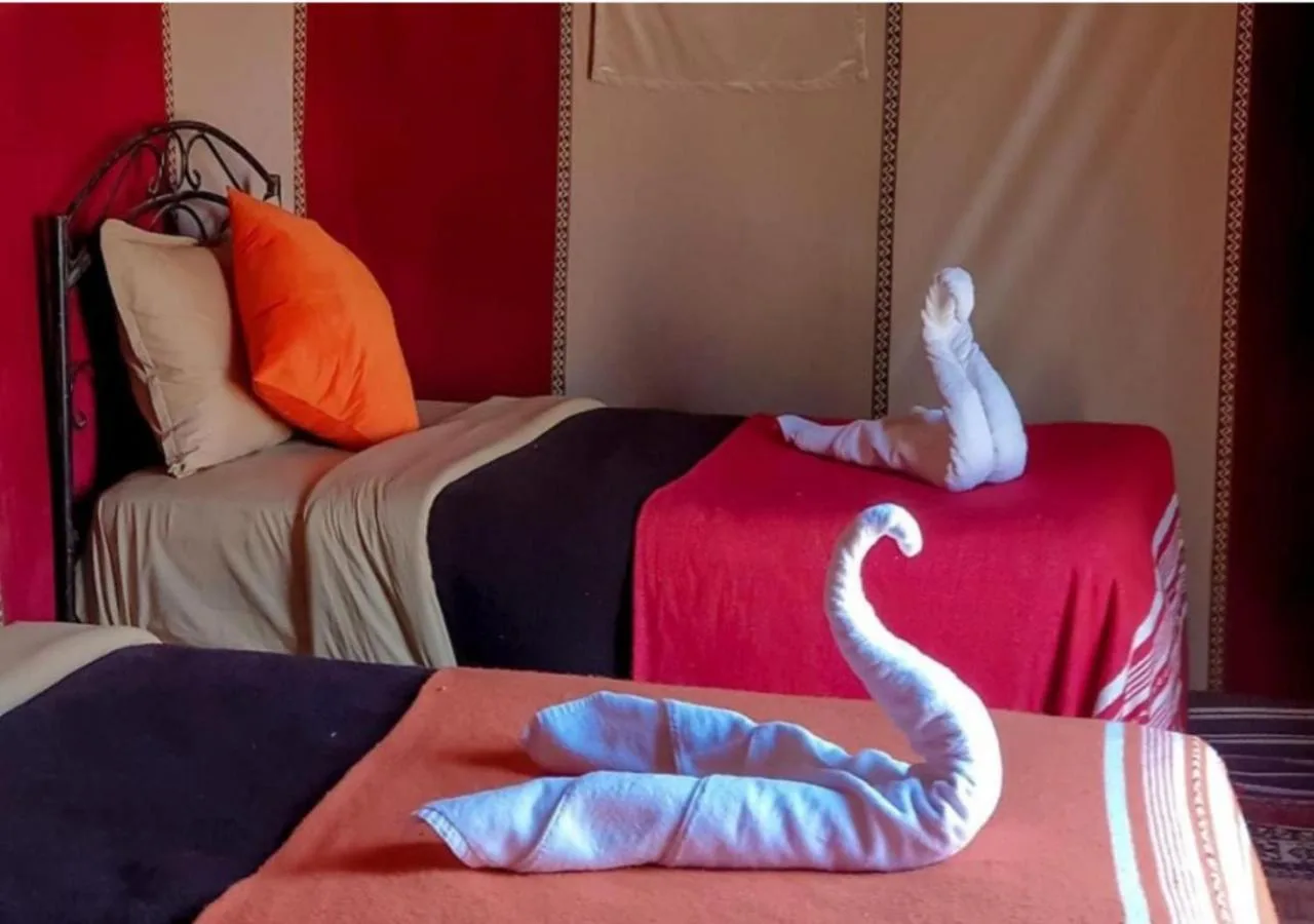 Twin beds inside Holiday Desert Camp Merzouga with neatly made linens and towel swan decoration