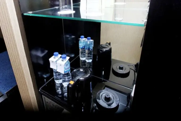 Mini bar area at Hotel Ciputra Semarang with bottled water, kettle, and glass shelving