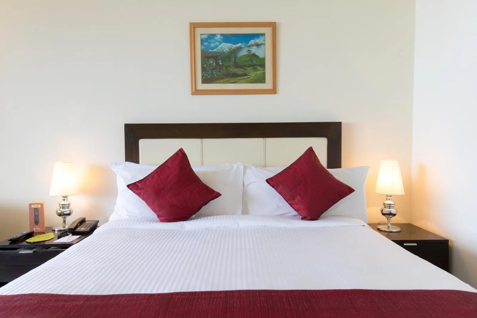 Lit king-size dans une chambre d’Hotel Himalaya Kathmandu avec coussins d’accent rouges et lampes de chevet.