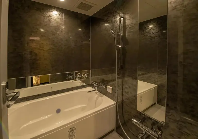 Salle de bains moderne de Hotel Kaguya à Himeji avec une baignoire, une douche et des murs texturés sombres.