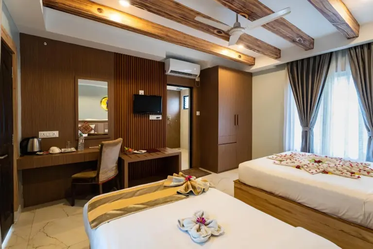 Intérieur d’une chambre à Hotel Seven Limited à Sauraha avec lits jumeaux, bureau, armoire et télévision murale.