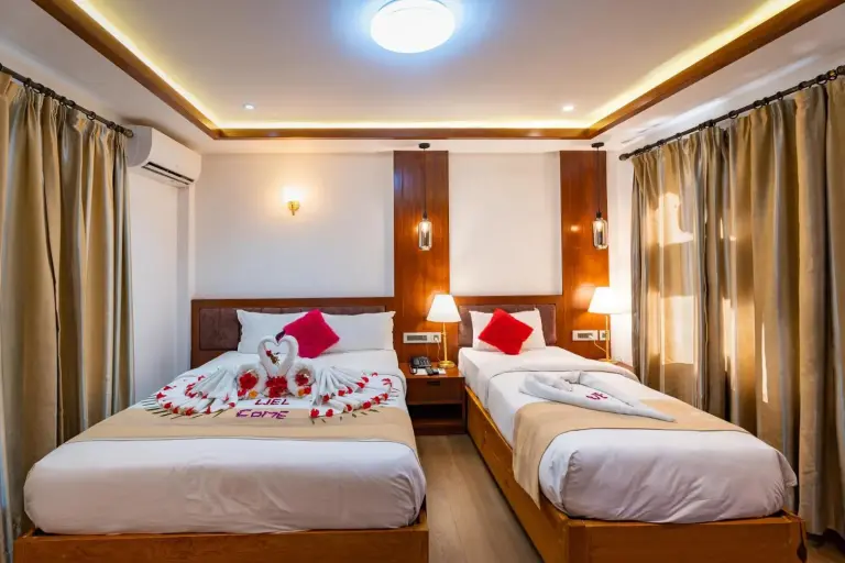 Chambre twin élégante à Hotel Seven Limited à Sauraha avec rideaux, poutres en bois et décoration florale sur le lit.