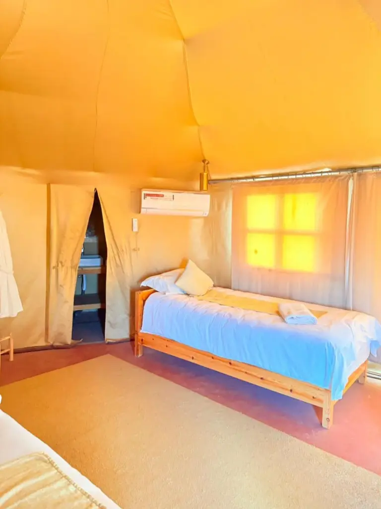 Hébergement sous tente avec lit simple au Houda Luxury Camp Merzouga à Merzouga avec climatisation et lumière chaude du désert.