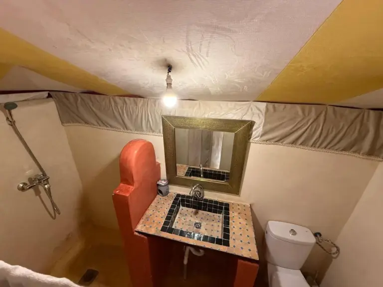 Salle de bains à l’intérieur d’une tente au Houda Luxury Camp Merzouga à Merzouga avec lavabo carrelé, miroir, toilettes et espace douche.