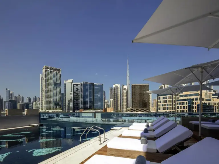 Terraza de la piscina exterior en Hyde Hotel Dubai en Dubai con tumbonas, sombrillas y vistas al skyline.