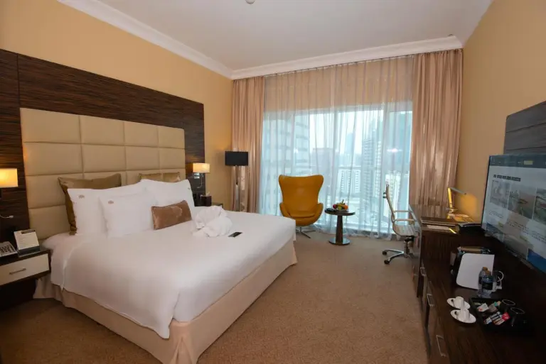 King guest room at Jannah Burj Al Sarab in Abu Dhabi with bed, TV, and panoramic window.