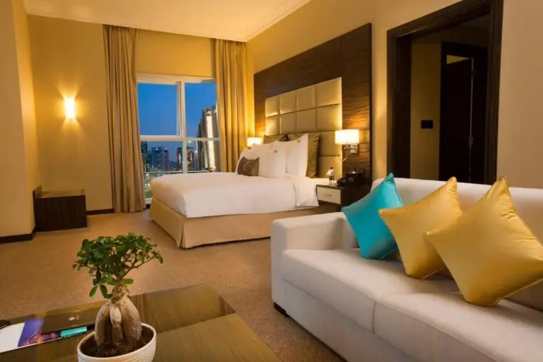 Suite-style room at Jannah Burj Al Sarab Abu Dhabi with sofa, bed, and evening city view.
