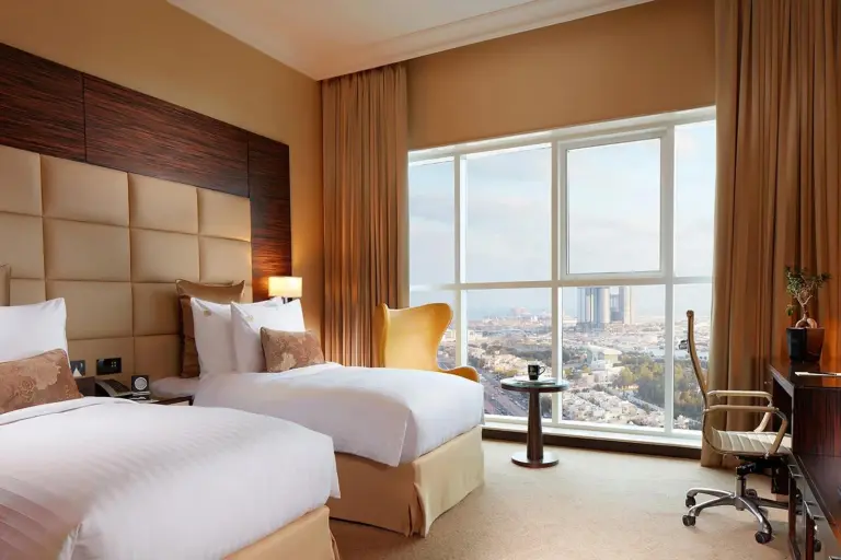 Twin guest room at Jannah Burj Al Sarab Abu Dhabi with two beds and a view of the skyline.