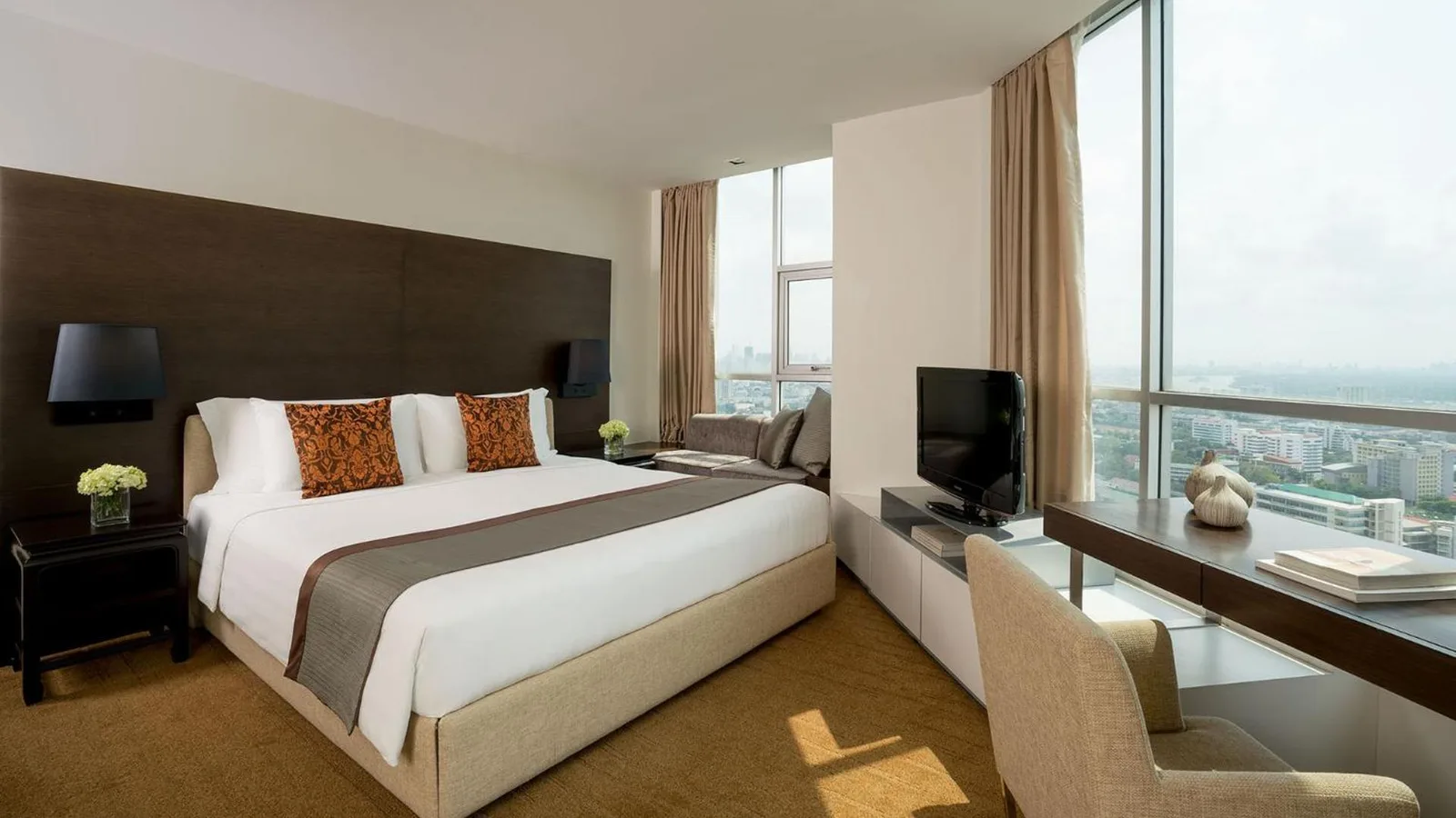 Spacious bedroom at JC Kevin Sathorn Bangkok Hotel with a king bed, desk, and panoramic windows.
