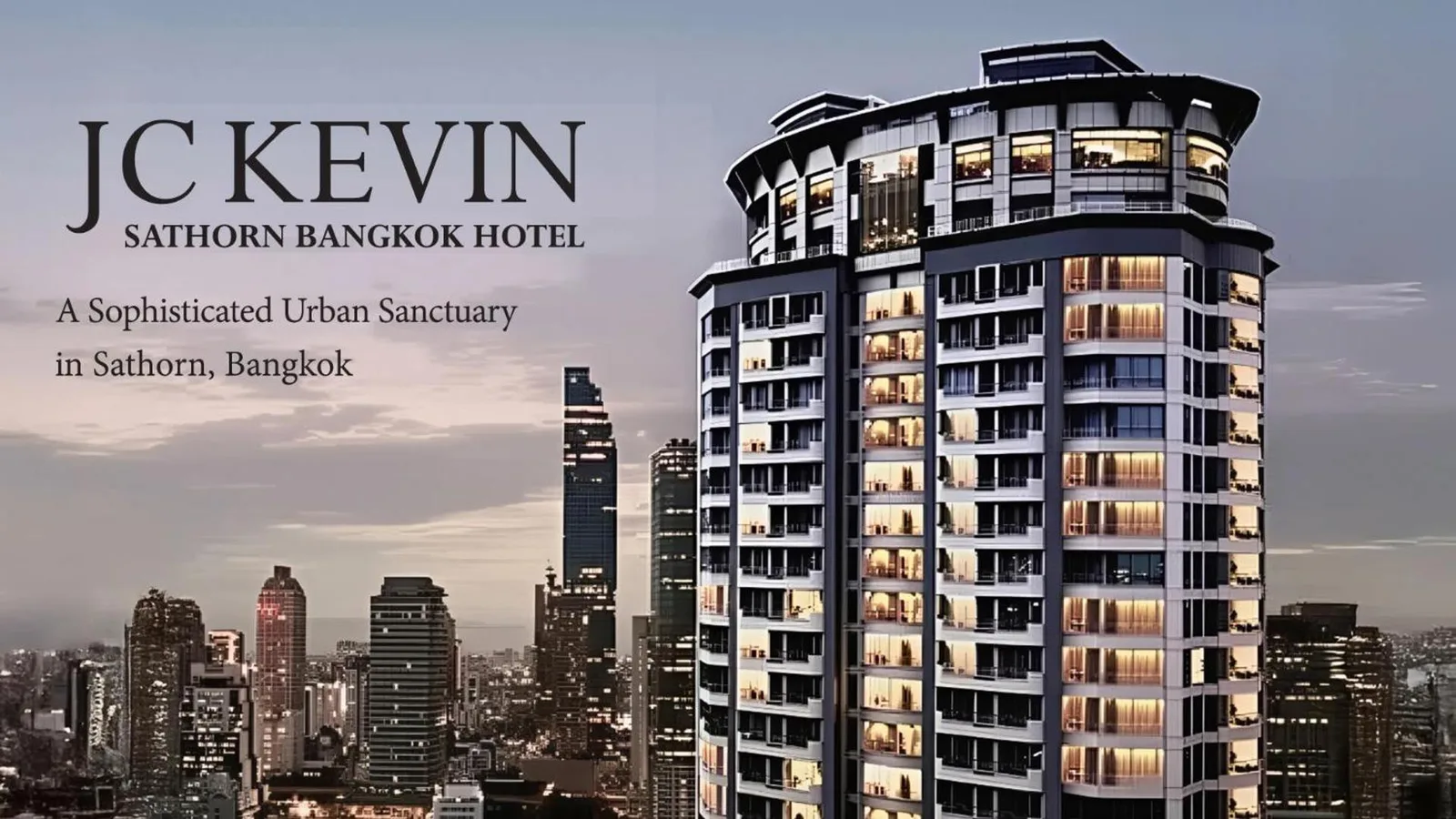 Exterior view of JC Kevin Sathorn Bangkok Hotel in Bangkok with the city skyline at dusk.
