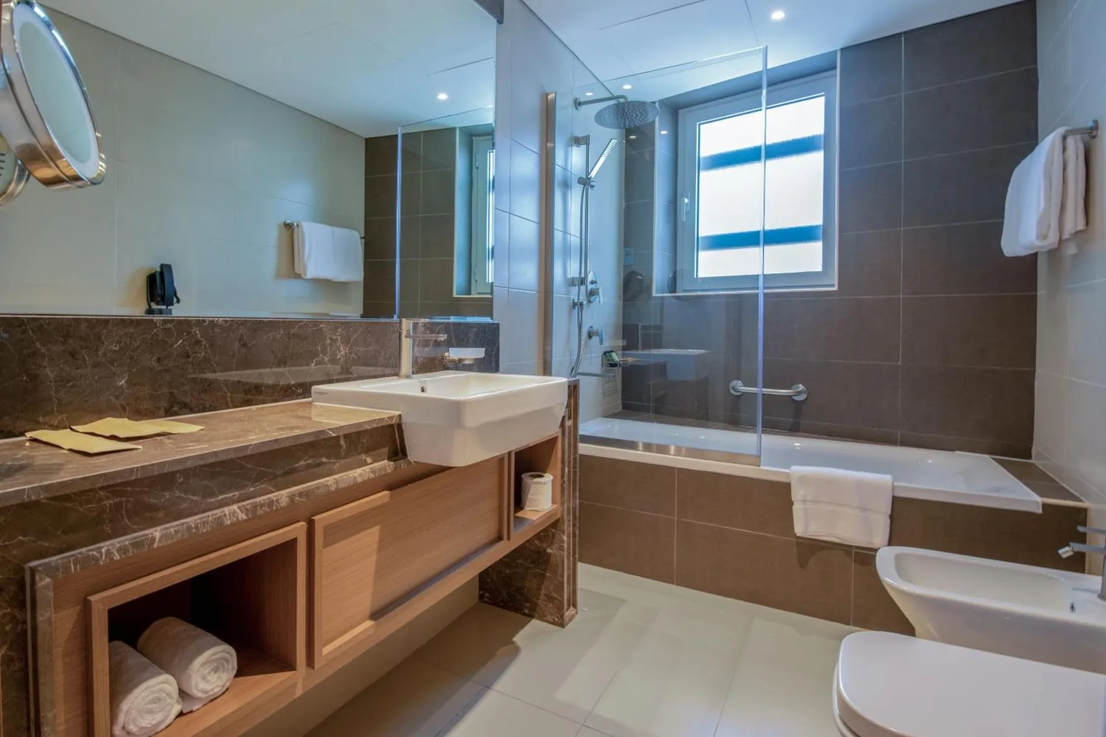 Bathroom at Jood Hotel Apartments Dubai with bathtub, vanity, and glass shower enclosure