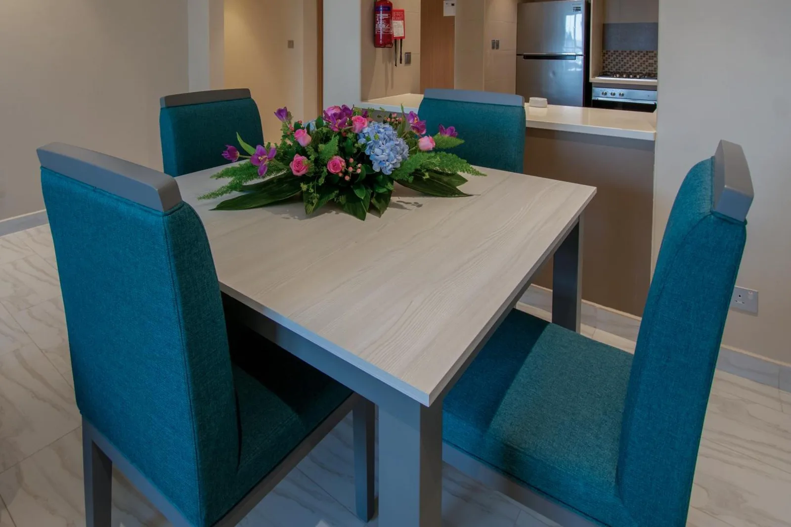 Dining area at Jood Hotel Apartments Dubai with teal chairs and a flower centerpiece