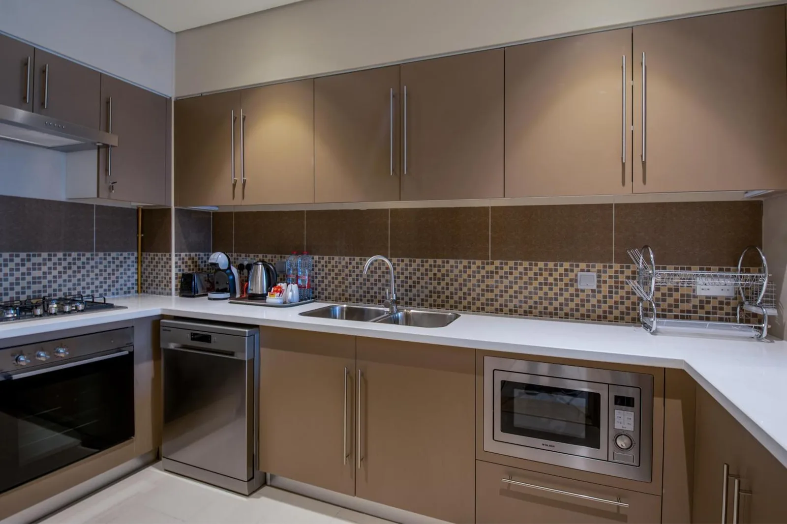 Modern kitchen counter at Jood Hotel Apartments Dubai with sink, stove, dishwasher, and microwave