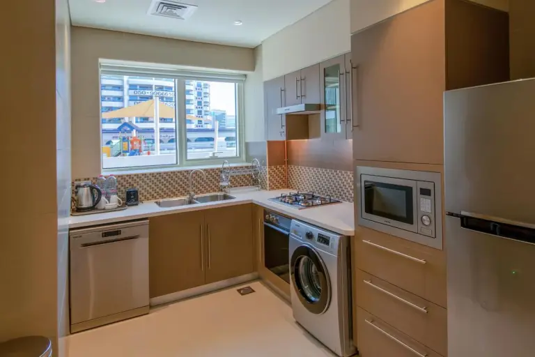 Fully equipped kitchen at Jood Hotel Apartments Dubai with appliances, cabinetry, and a window view