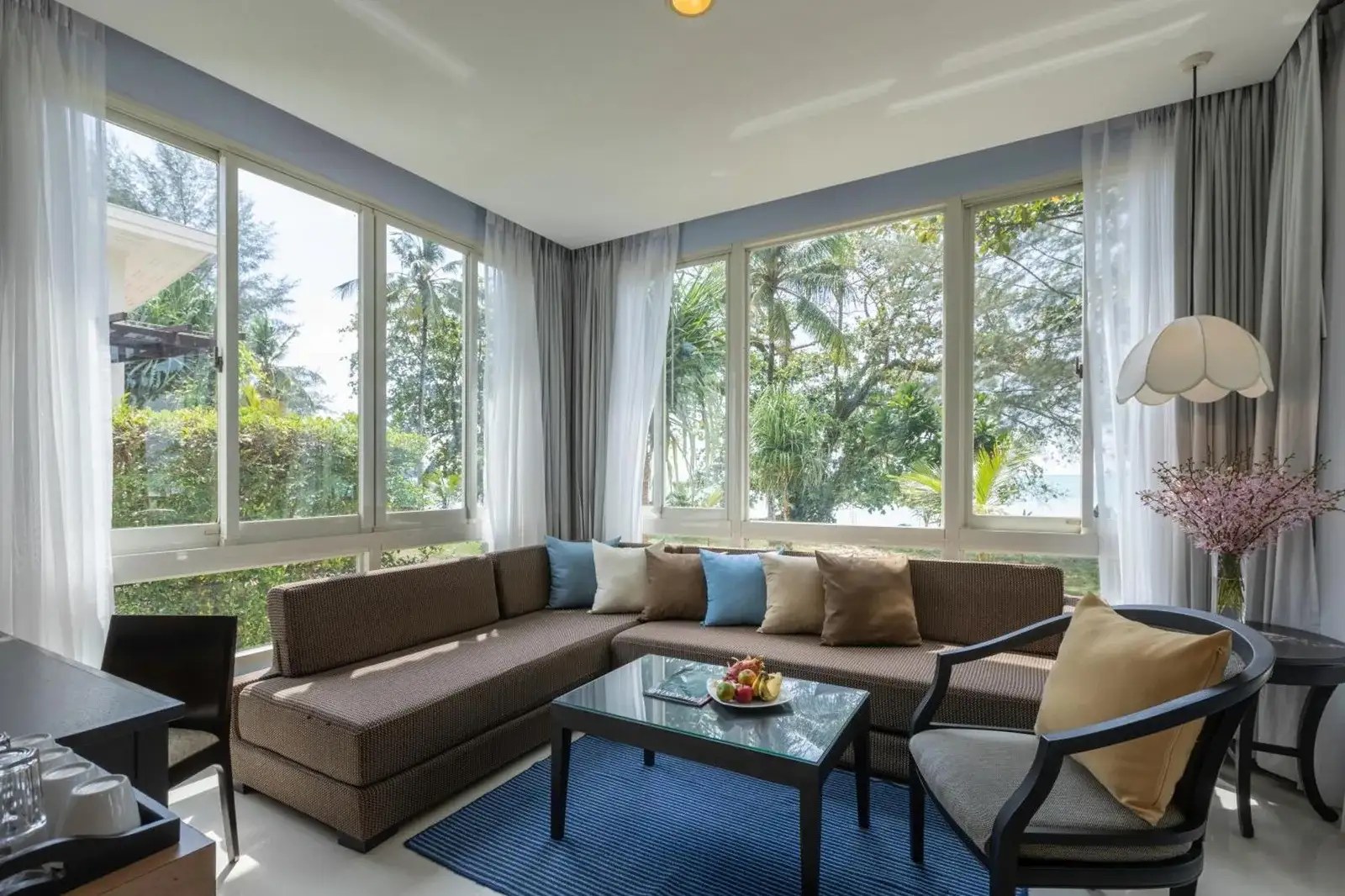 Salón luminoso en Kantary Beach Hotel Villas & Suites en Khao Lak con sofá seccional, grandes ventanales y vistas al jardín