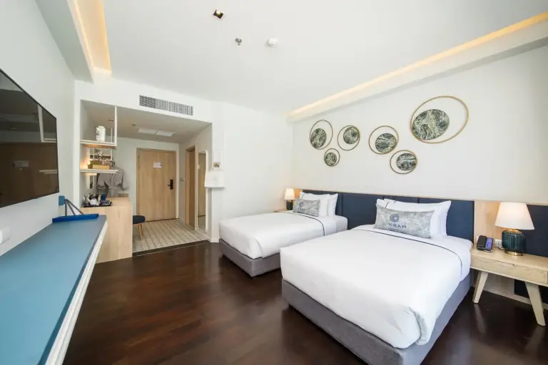 Spacious twin room at Kram Pattaya hotel in Pattaya with two beds, work area, and entrance view
