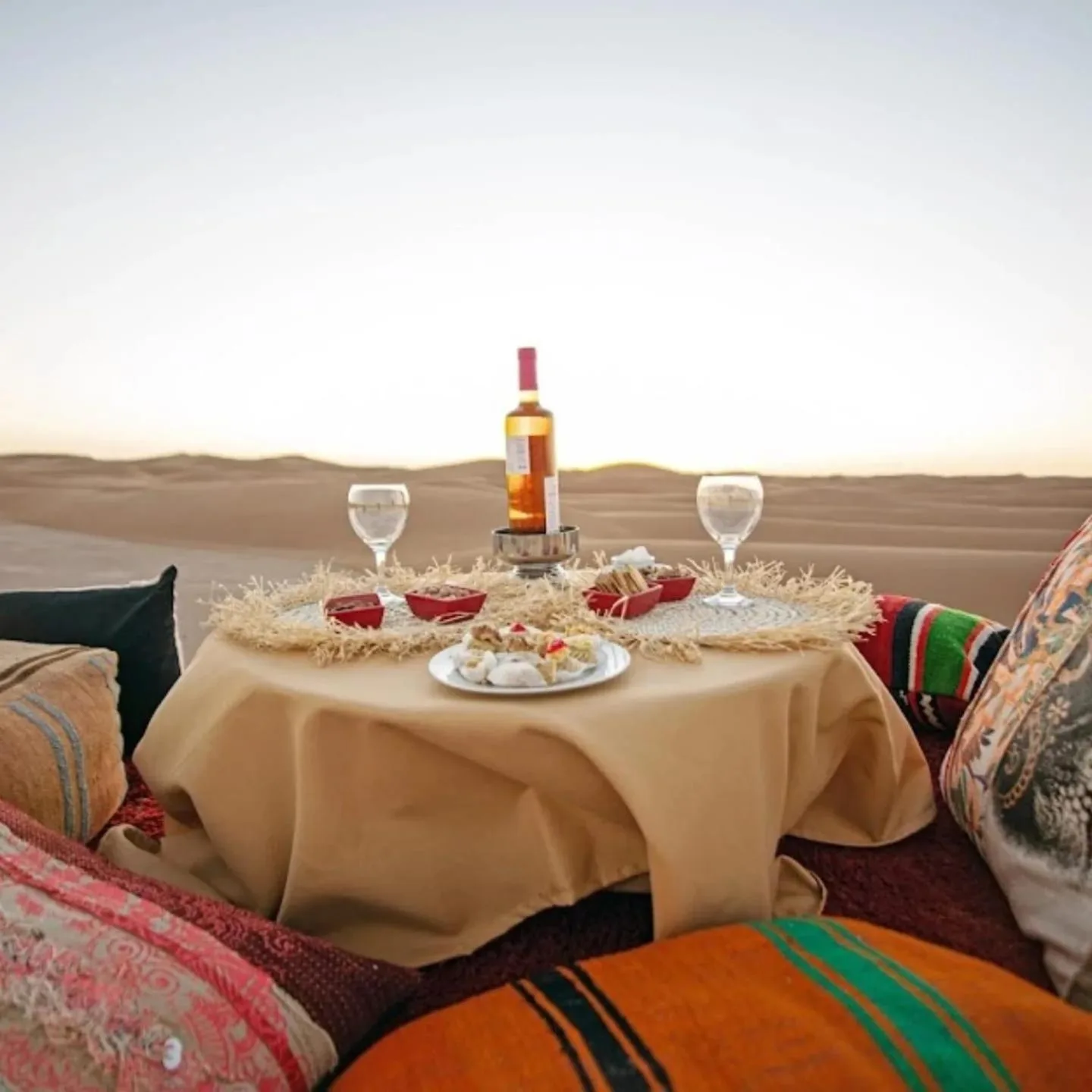 Eine Lounge im Picknick-Stil in der Wüste im Lana Camp Merzouga in Merzouga mit Wein, Gläsern und Kissen.