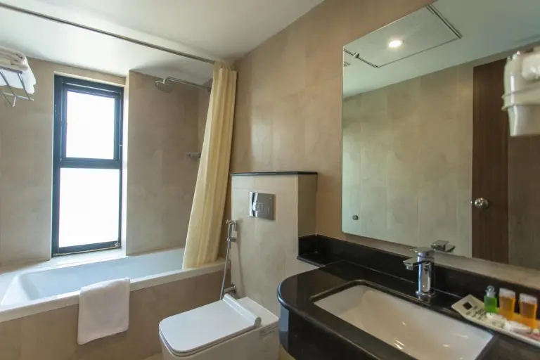 Baño en Landmark Pokhara en Pokhara con bañera, inodoro, lavabo y paredes de azulejos beige.