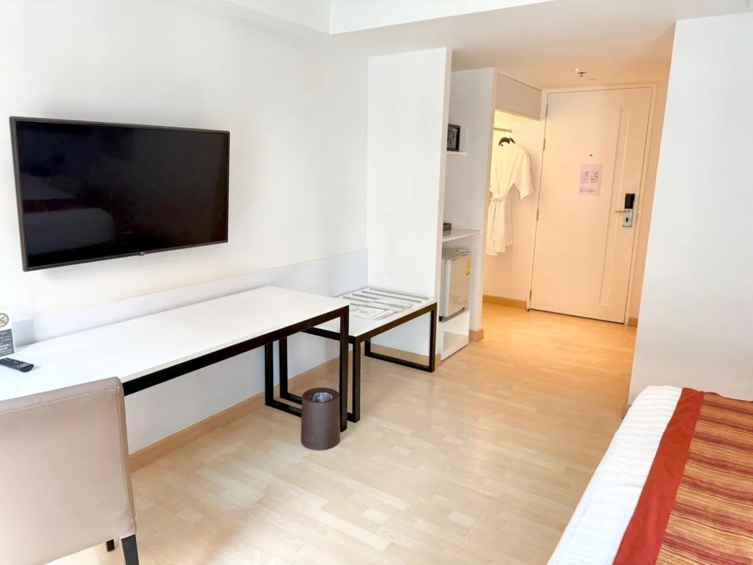 Modernes Gästezimmer im Le D'Tel Bangkok mit Bett, Schreibtisch, TV und Eingang zum Bad.