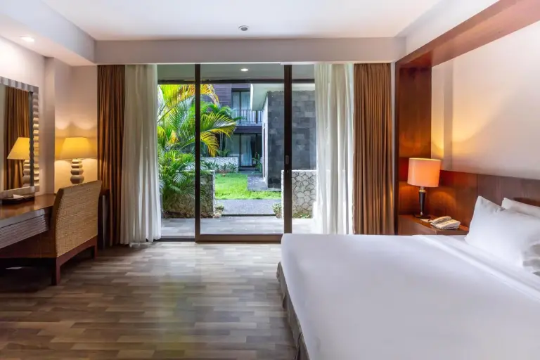 Deluxe bedroom at Le Grande Bali in Uluwatu with a king bed, work desk, and sliding glass doors opening to the garden.