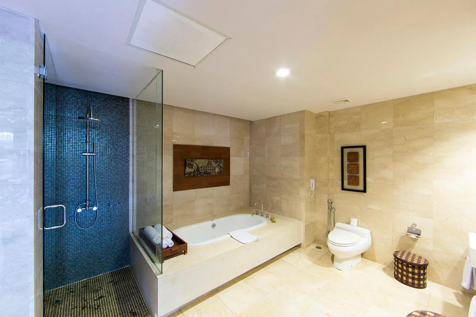 Spa-style bathroom at Le Grande Bali in Uluwatu with a glass shower, soaking tub, and beige tile walls.