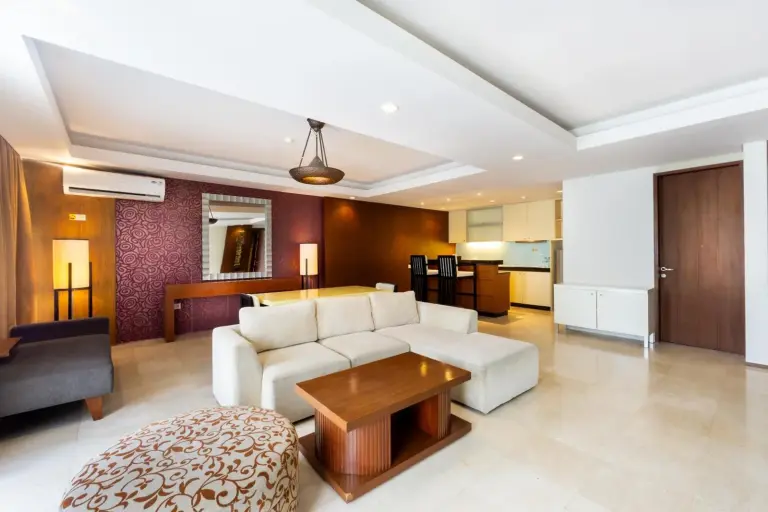 Suite living area at Le Grande Bali in Uluwatu with a sectional sofa, wooden coffee table, and open-plan kitchen.