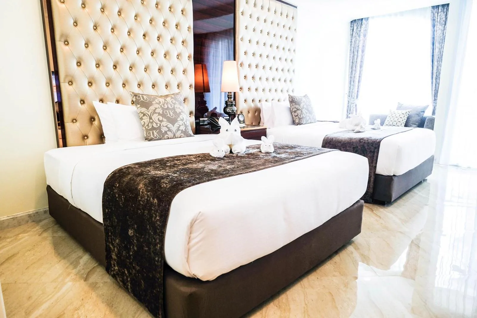 Vista en ángulo de una habitación doble en LK Grand Empire en Pattaya con ropa de cama de lujo y ventanas luminosas