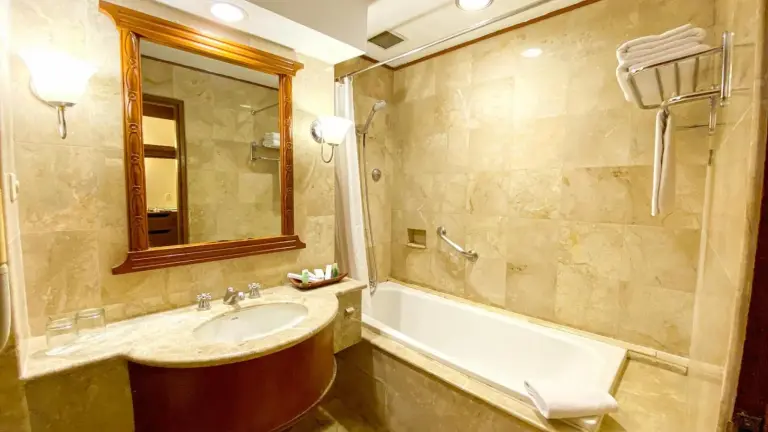 Badezimmer im Lorin Solo Hotel mit Badewanne, Waschbecken, Spiegel und beigefarbenen Steinfliesen in Surakarta