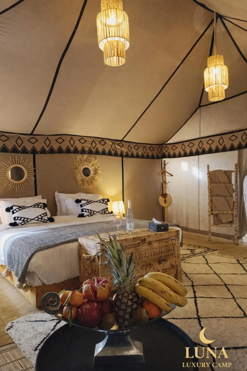 Intérieur d’une tente de luxe à Luna Luxury Camp Merzouga à Merzouga avec un lit double, un éclairage chaleureux et une décoration désertique élégante.