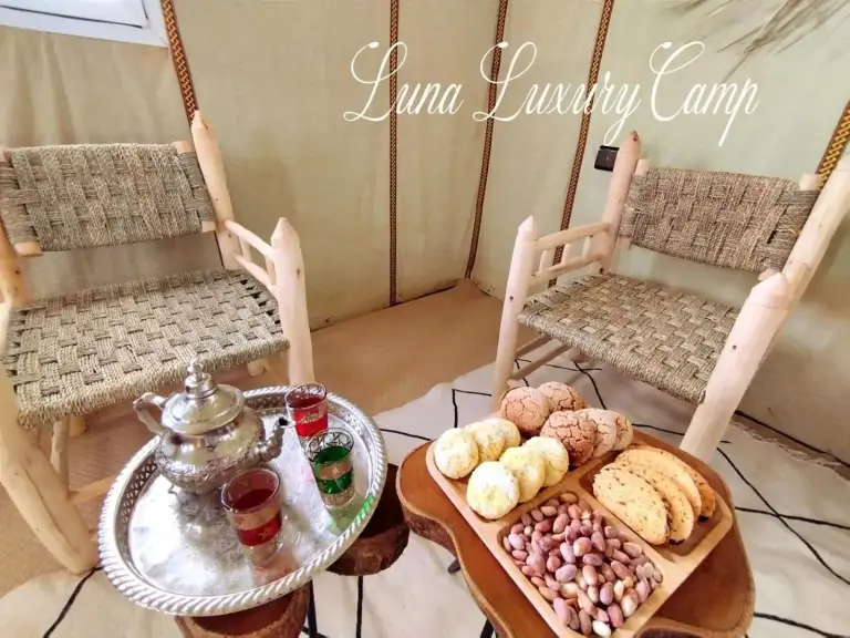 Coin salon relaxant à Luna Luxury Camp Merzouga à Merzouga avec des chaises en osier, des fruits et de petites tables.