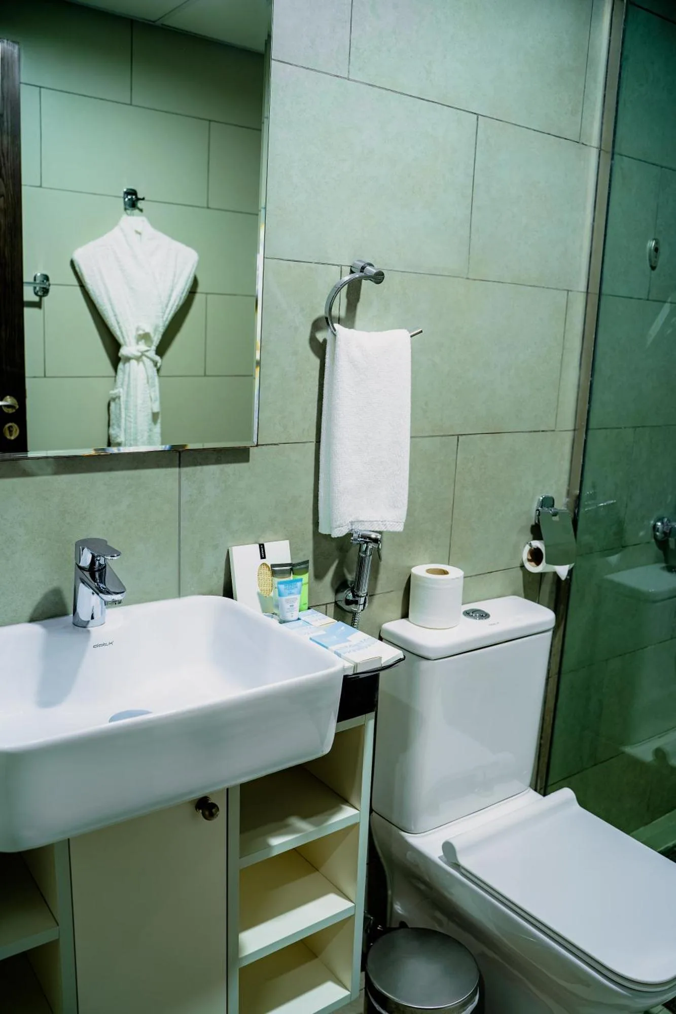 Kompaktes Badezimmer im Luxe Grand Hotel Apartments in Schardscha mit Toilette, Waschbecken, Spiegel, Handtuch und Glasdusche.