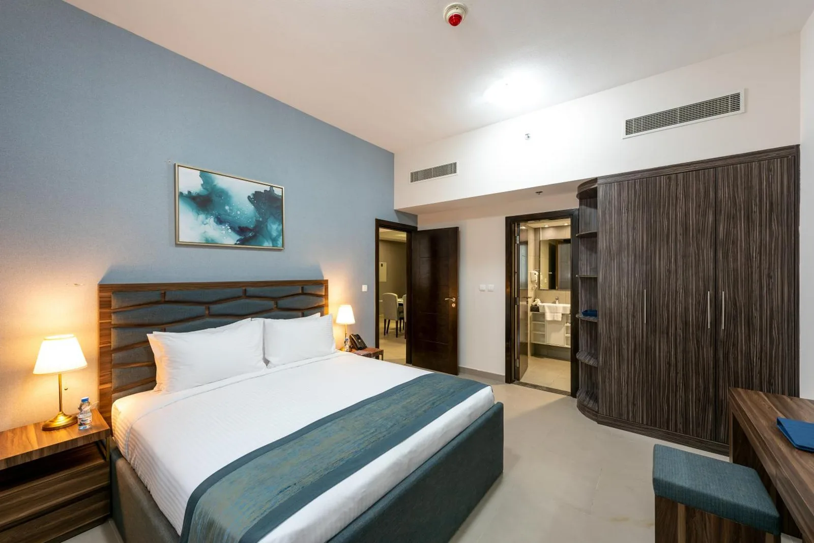 Elegantes Schlafzimmer im Luxe Grand Hotel Apartments in Schardscha mit Doppelbett, Nachttischlampen und Fenstervorhängen.