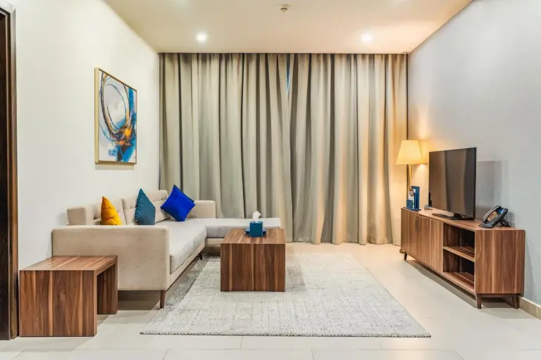 Stilvolles Wohnzimmer im Luxe Grand Hotel Apartments in Schardscha mit Sofa, TV-Möbel, Couchtisch und Vorhängen.