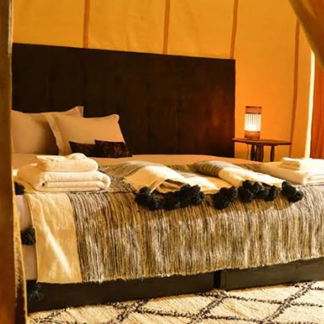 Warm-lit double bed inside a tent room at Luxury Camp View in Merzouga