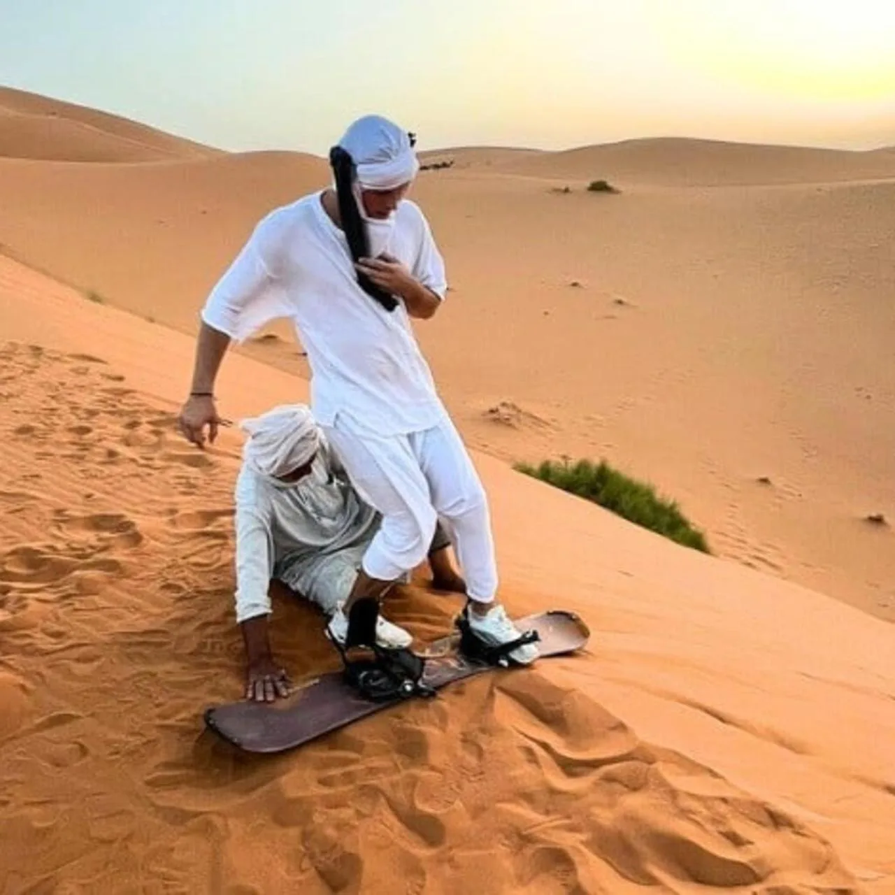 Two people practicing sandboarding on a dune near Luxury Camp View in Merzouga
