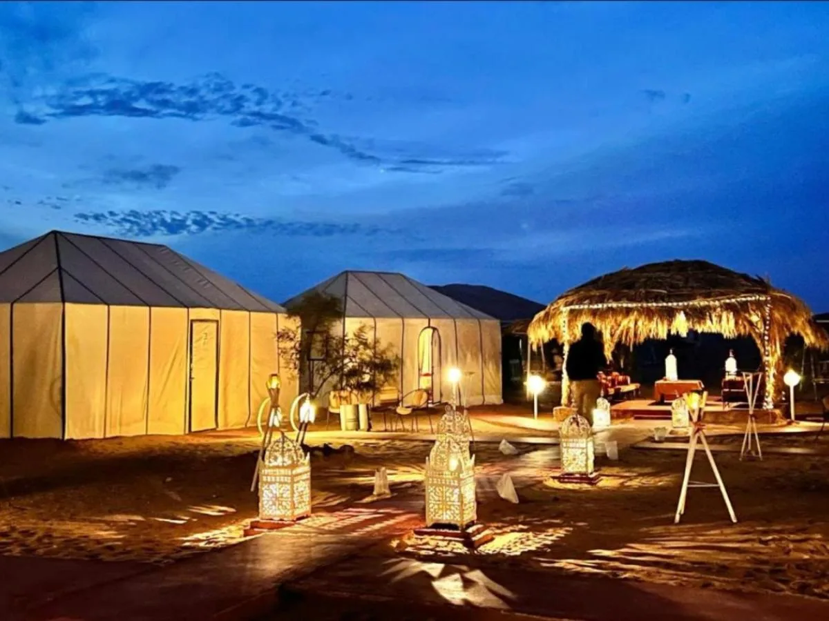 Beleuchtete Zelte und ein Außen-Loungebereich im Luxury Dune's Camp in Merzouga, Marokko, in der Dämmerung.