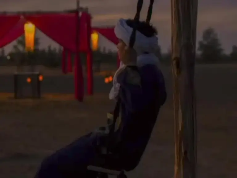 Eine Person sitzt bei Sonnenuntergang auf einer Schaukel im Luxury Dune's Camp in Merzouga, Marokko.