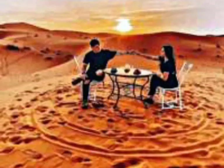 Gäste speisen bei Sonnenuntergang auf dem Sand im Luxury Dune's Camp in Merzouga, Marokko.