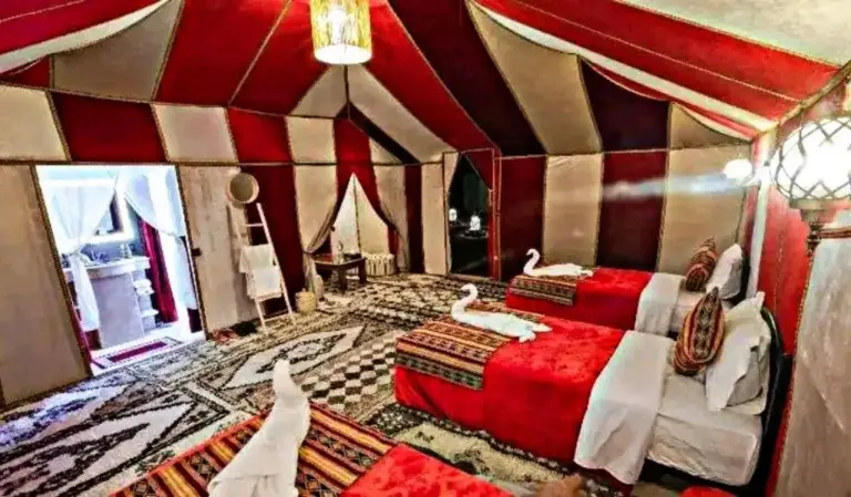 Innenraum eines Zimmers mit zwei Betten im Zelt im Luxury Dune's Camp in Merzouga, Marokko, mit bunten Teppichen und Dekor.