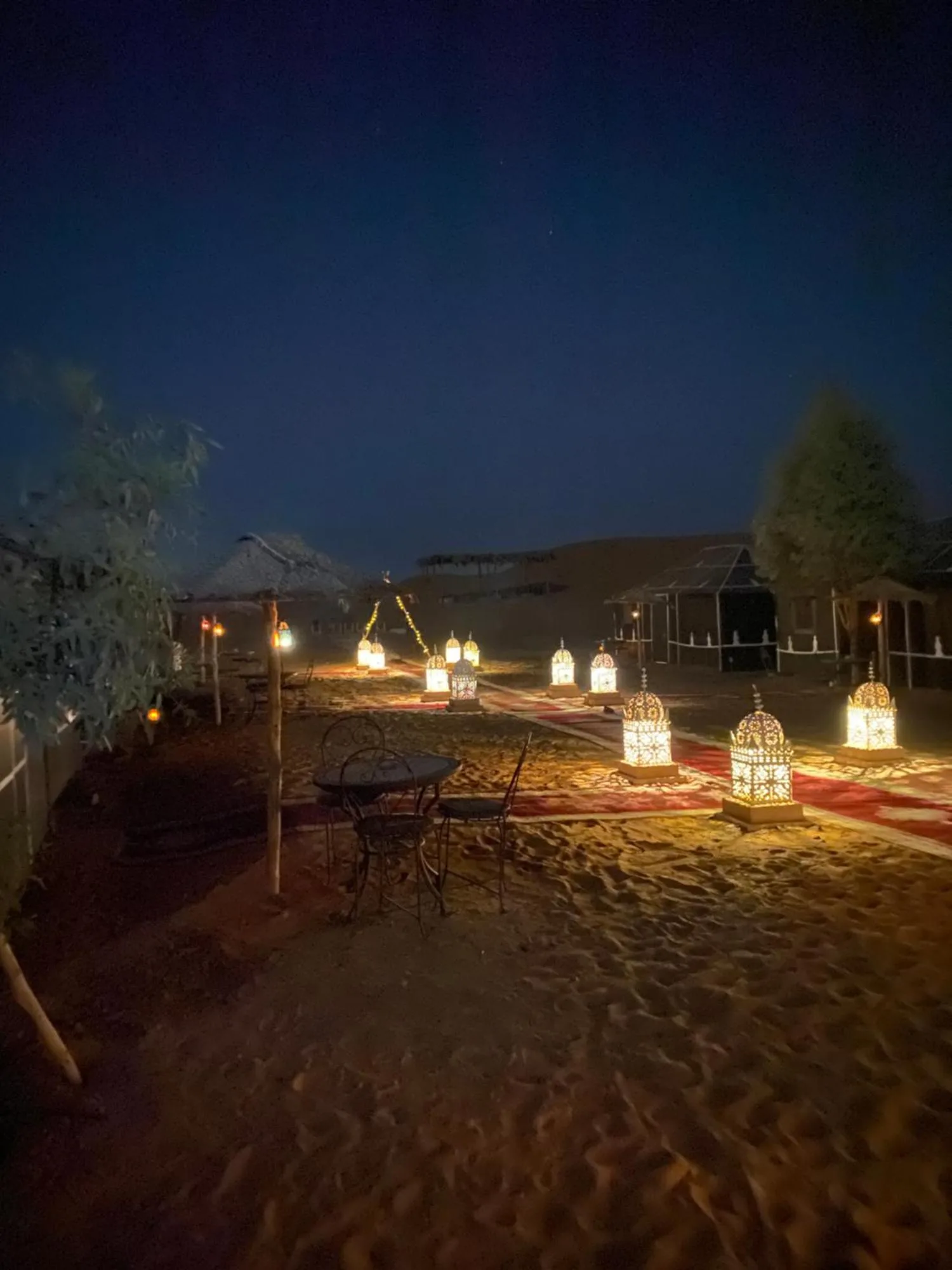 Vue nocturne des abords du camp au Luxury Merzouga Stars Camp à Merzouga avec éclairage de lanternes et espaces assis.