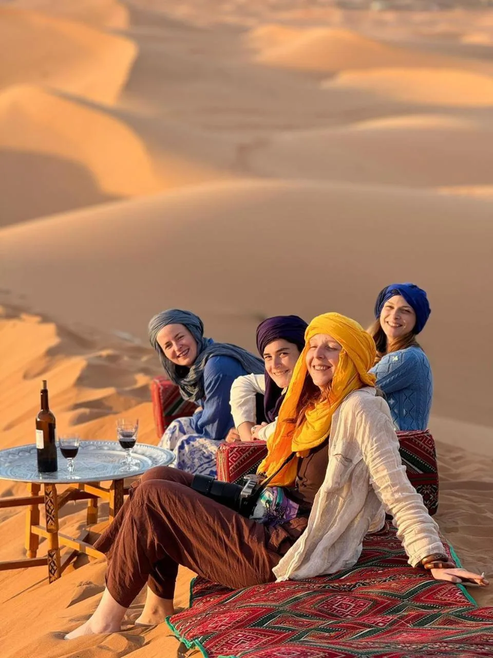Groupe de femmes se détendant sur des coussins dans les dunes au Luxury Merzouga Stars Camp à Merzouga avec des boissons sur une petite table.