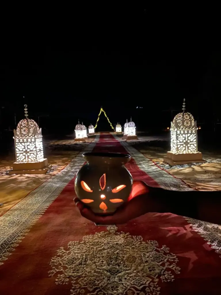 Allée du soir illuminée au Luxury Merzouga Stars Camp à Merzouga avec lanternes décoratives et tapis rouges.