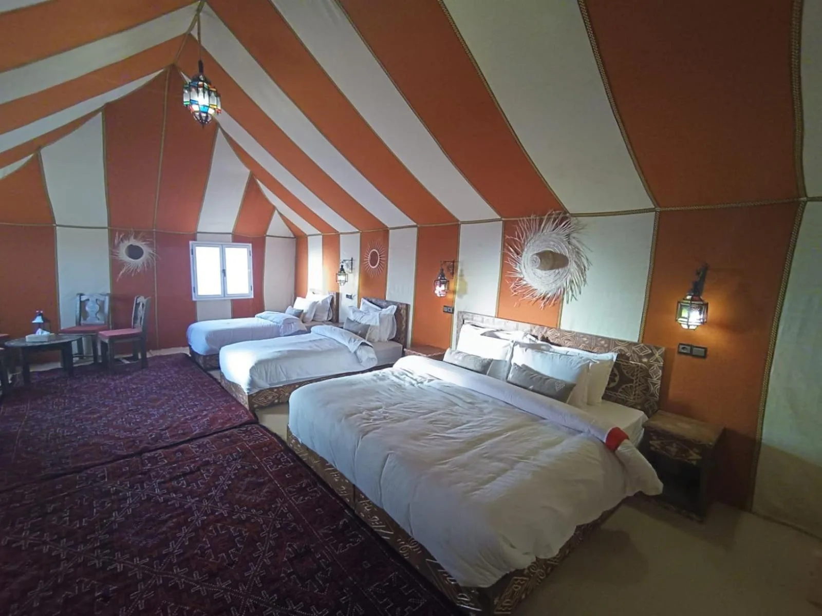 Orange striped triple tent room at Luxury Nomadic Tented Camp in Merzouga with three beds and carpeted floor.