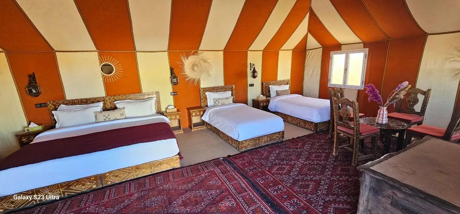 Large triple suite at Luxury Nomadic Tented Camp in Merzouga with three beds, dining table, and desert decor.